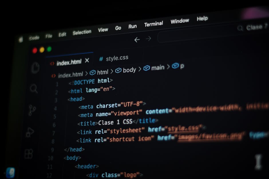 A close-up of a person's hands typing on the keyboard of a MacBook laptop placed on a dark table. The laptop screen displays lines of code in a text editor with a dark background, featuring various sy